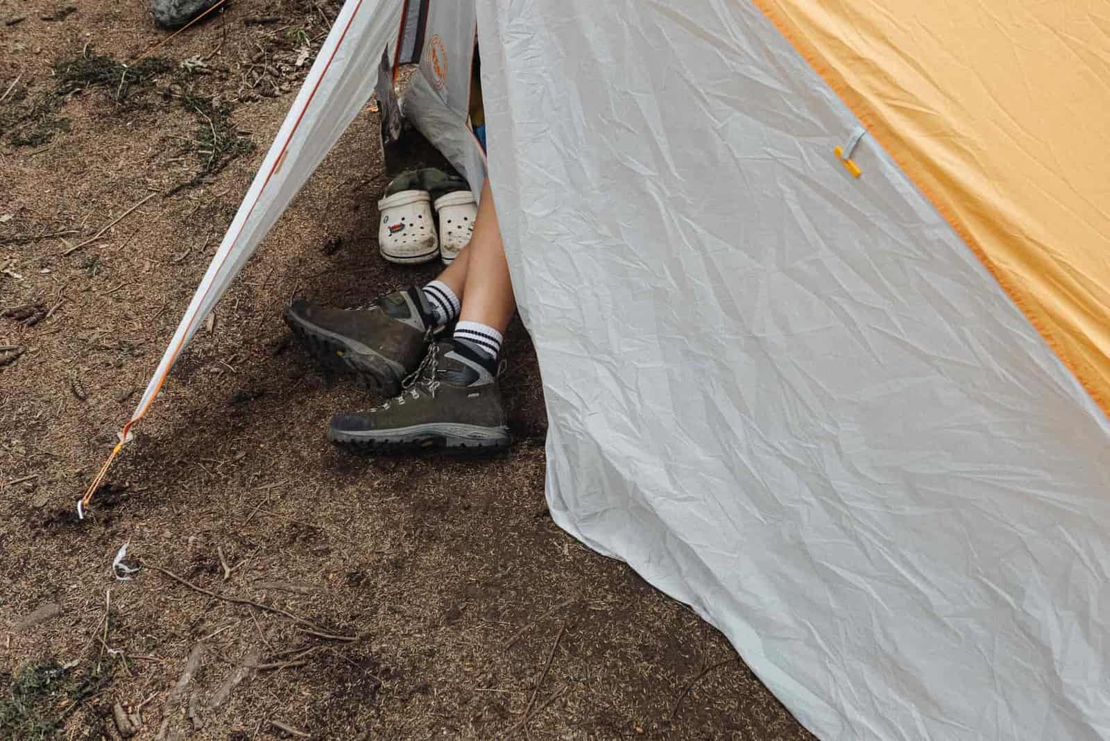 Hiking boots on the ground beside a tent at a campsite
