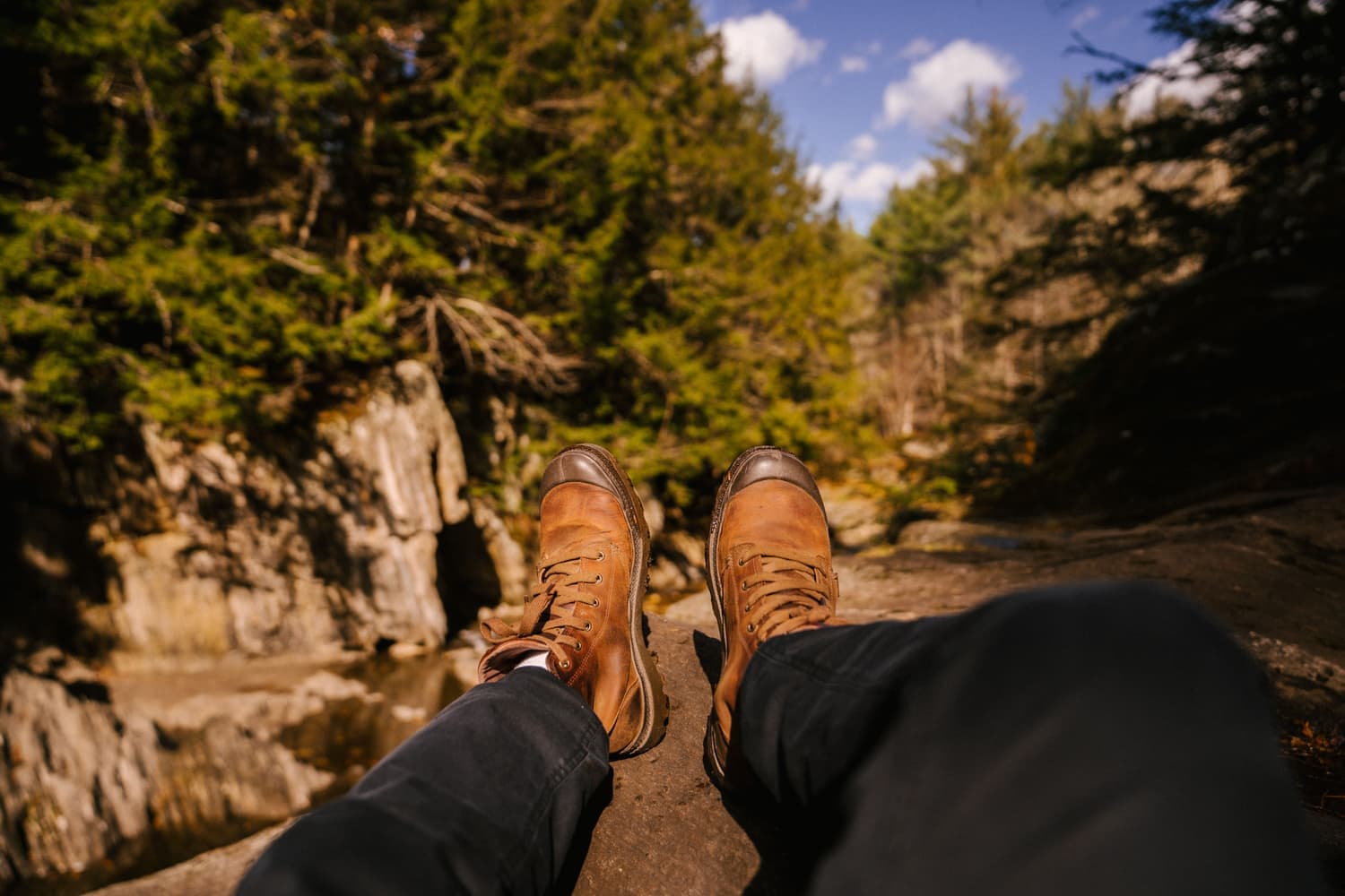 A hiker resting with leather boots up beside a mountain stream