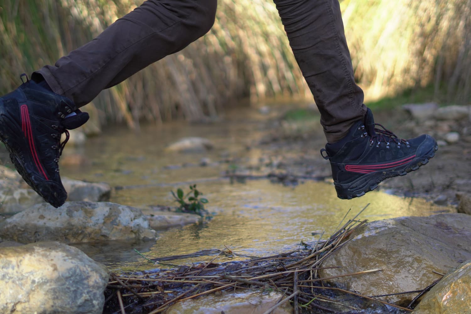 A hiker in trail shoes stepping over a shallow creek