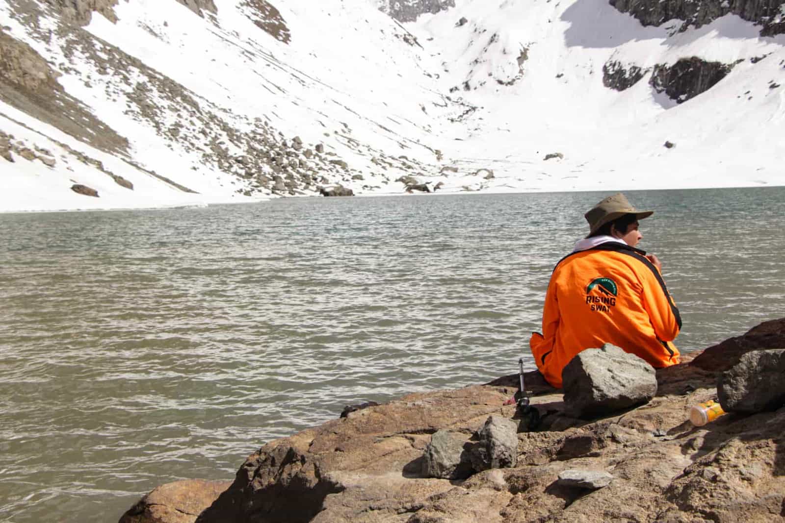 A hiker resting on rocks beside a snowy mountain lake