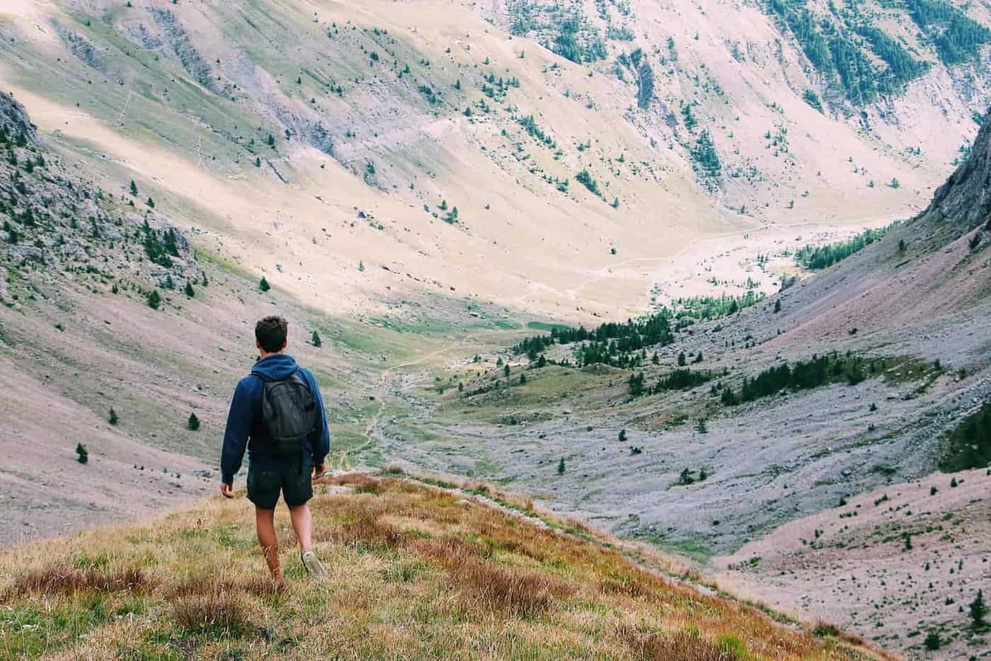 A hiker with a backpack walking into a wide mountain valley