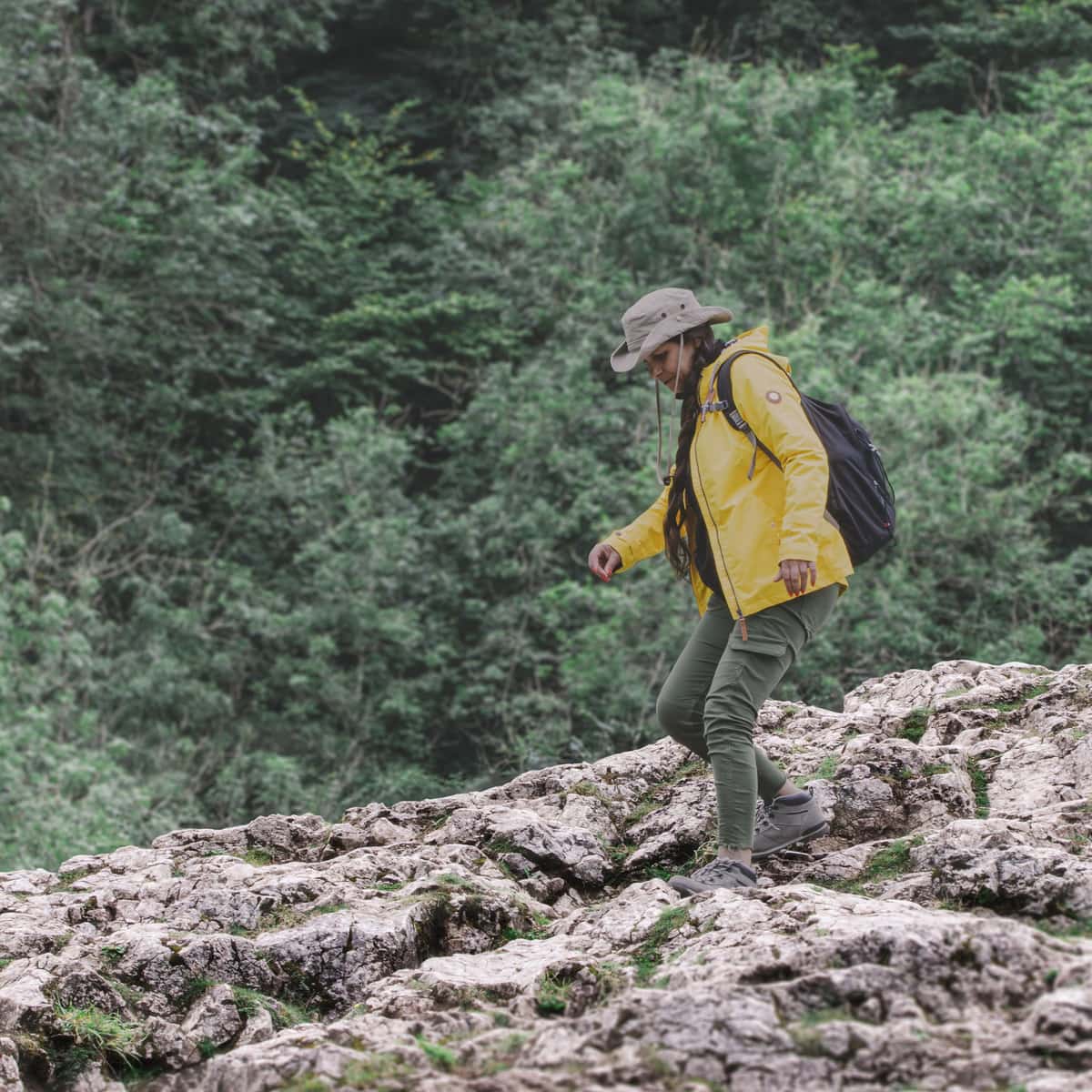 A hiker in a yellow jacket stepping across rocks in a forest