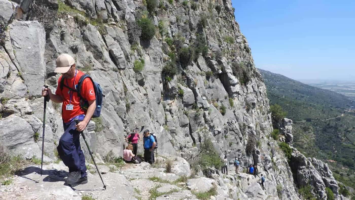 Hikers with trekking poles on a steep, rocky mountain path