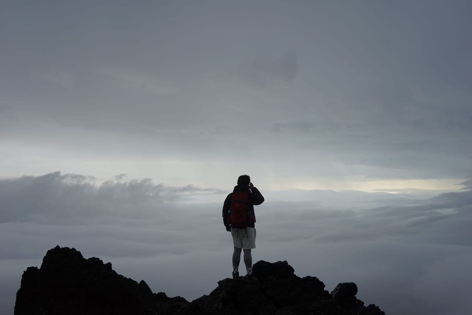 A lone hiker standing on a peak above the clouds
