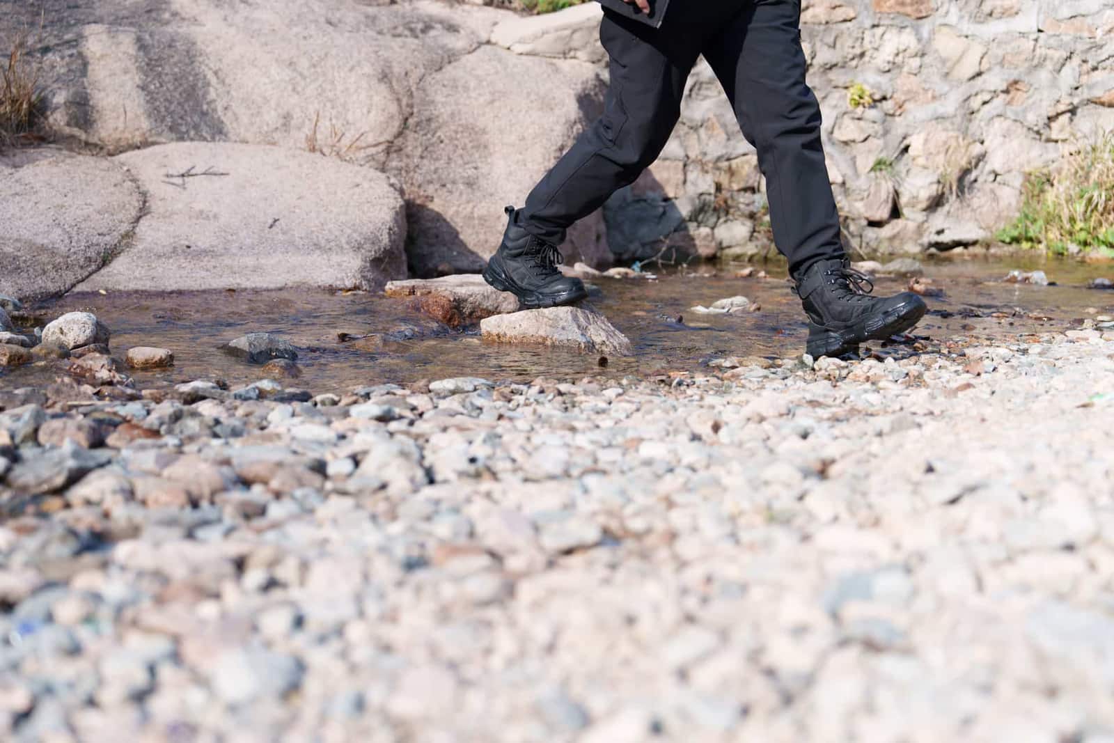 A hiker in boots stepping across a shallow, rocky stream