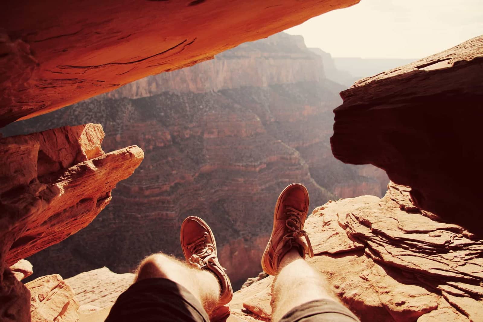 A hiker's legs and shoes resting at the edge of a canyon