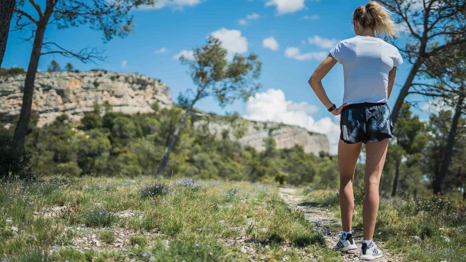 A woman in shorts and trail shoes on a sunny mountain path