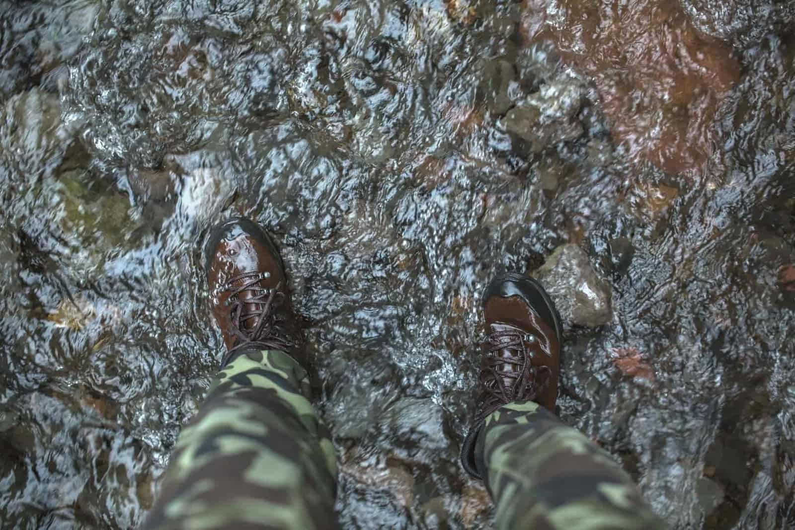 A person standing in a river in brown hiking boots