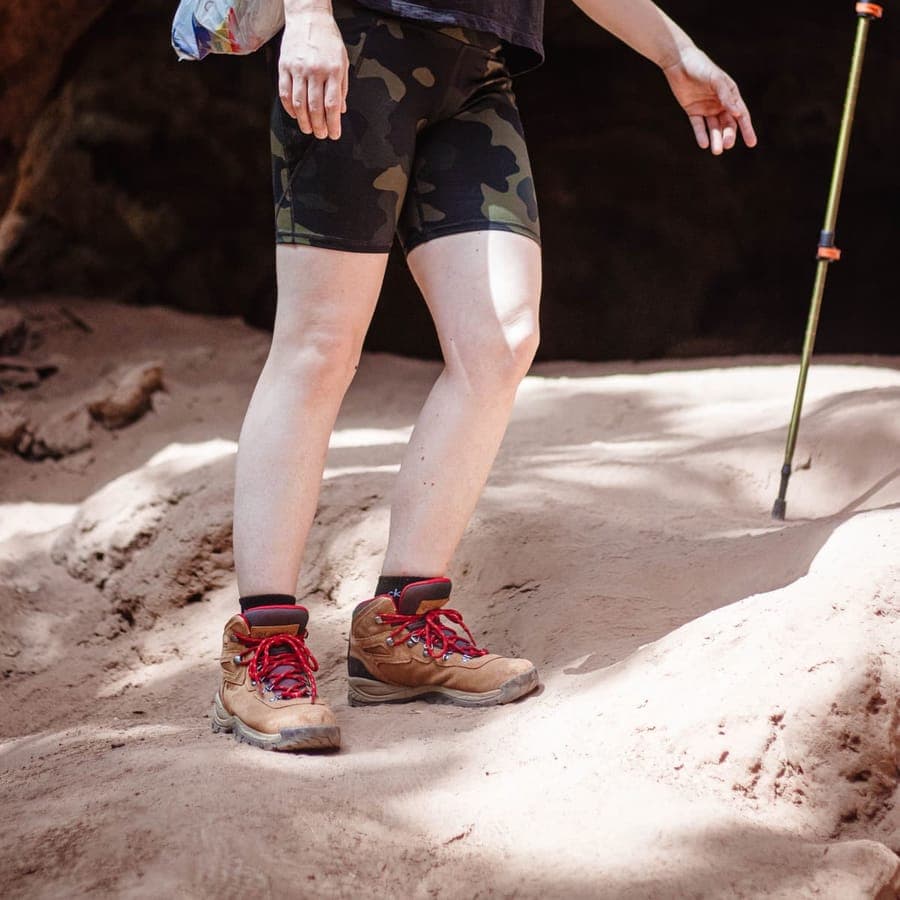 A hiker in shorts and hiking boots on sandy ground with a trekking pole