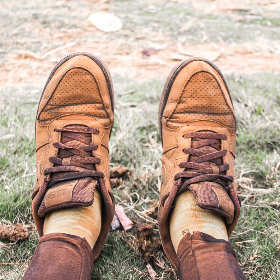 A pair of worn brown lace-up shoes on grass, seen from above