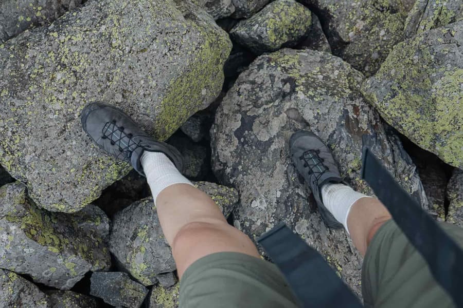 A hiker's feet in trail shoes on moss-covered rocks